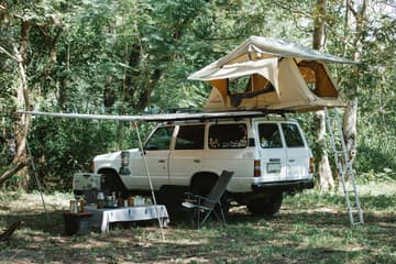 White off-road SUV with rooftop tent set up in a lush forest clearing, showcasing adventure vehicle preparation