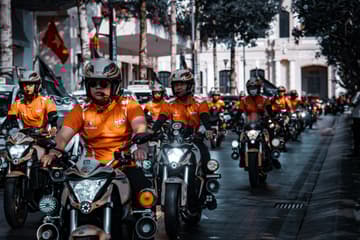 Group of motorcycle riders in orange gear riding through a street during a large urban motorcycle gathering